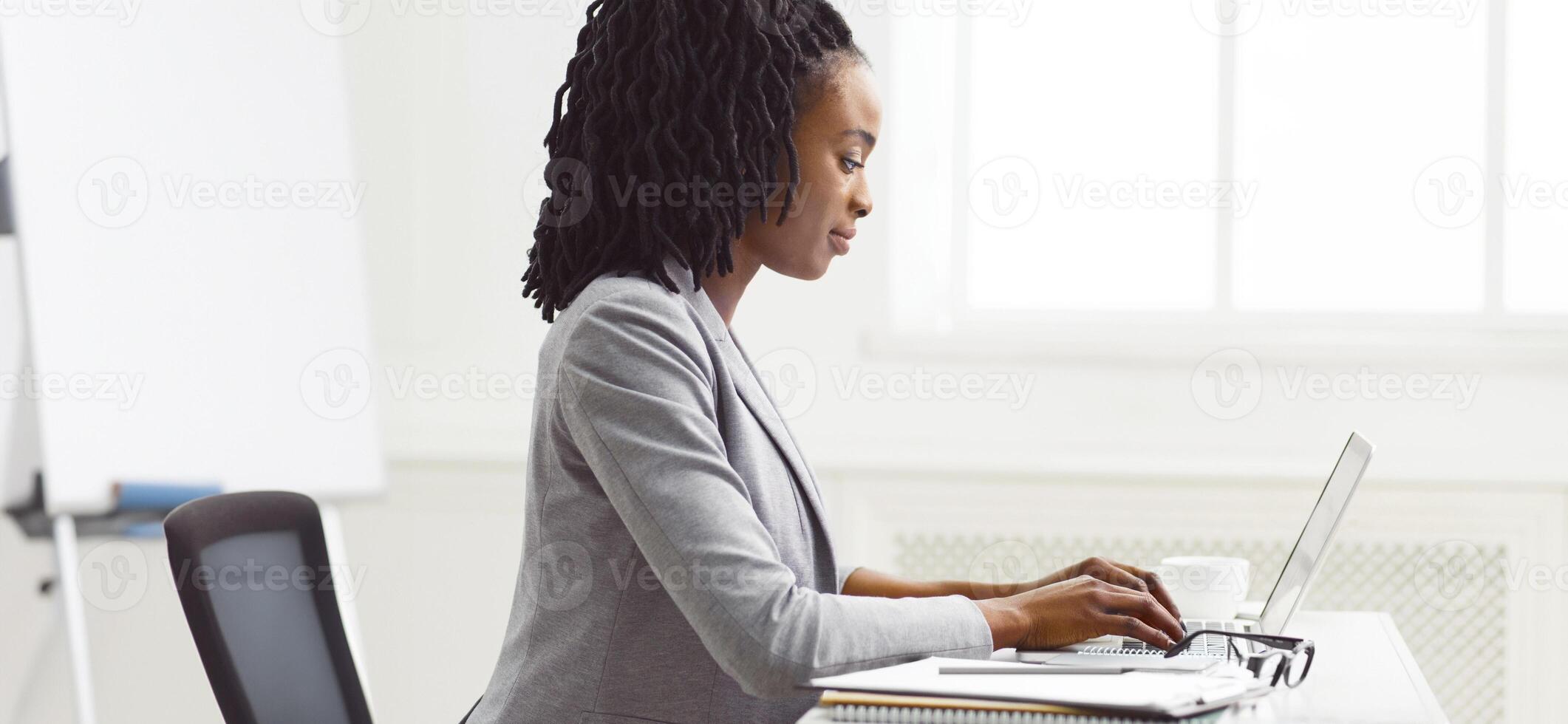A focused African American lady is working on her computer at her office desk. The scene is professional and organized, emphasizing concentration and business efficiency. photo