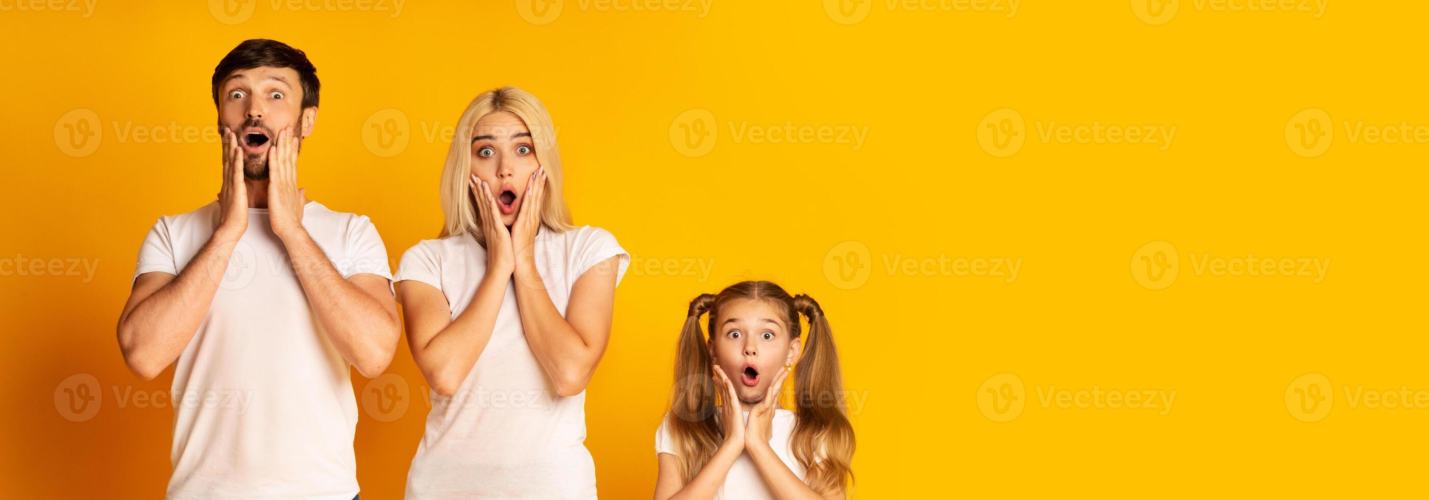 A family is displaying expressions of shock and excitement against a vibrant yellow backdrop. The adults and child appear astonished, with hands on their faces and wide eyes, copy space photo