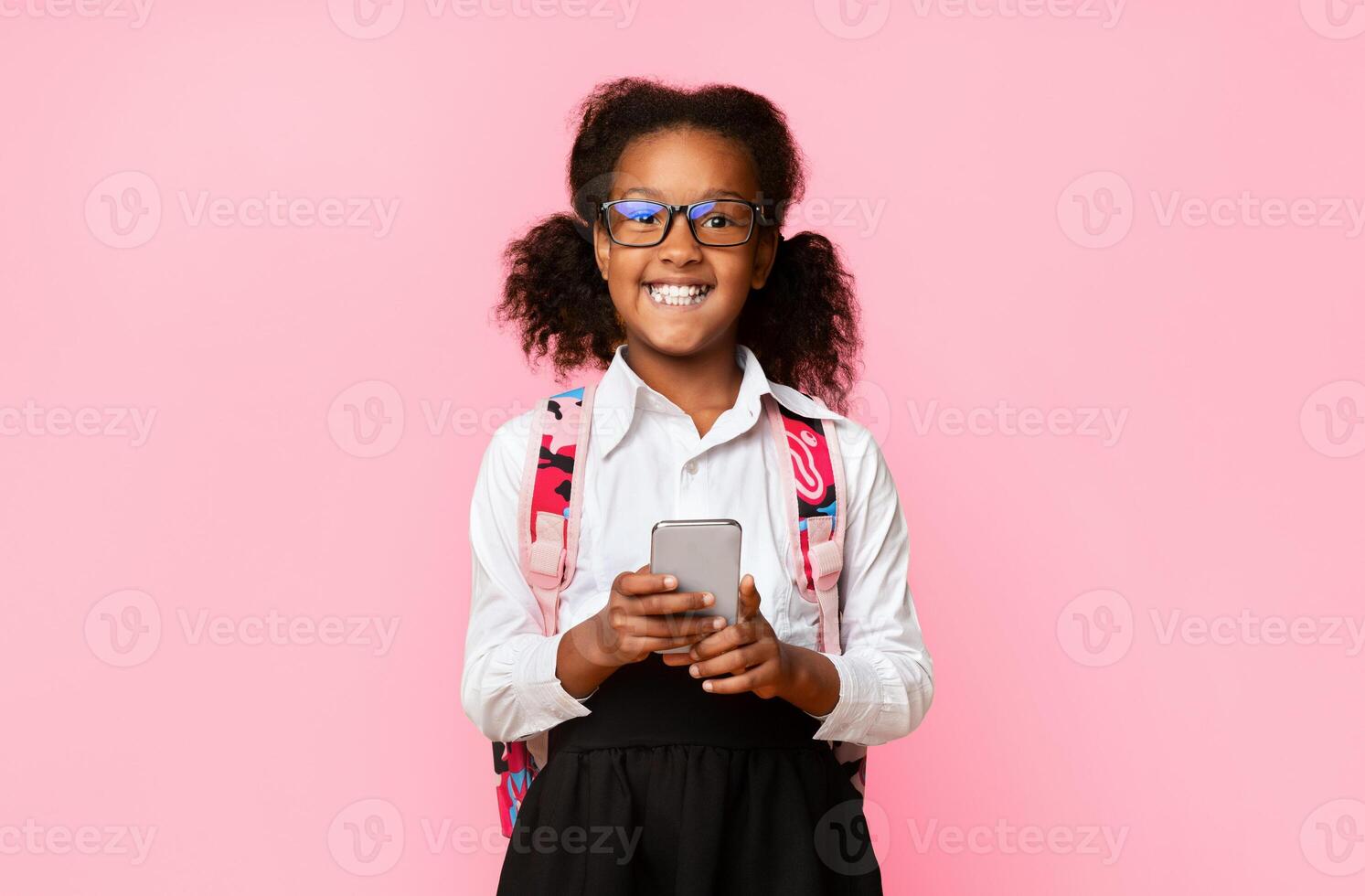 Mobile Game. Happy African Schoolgirl Using Smartphone Playing Online Games At School Posing On Yellow Studio Background. photo