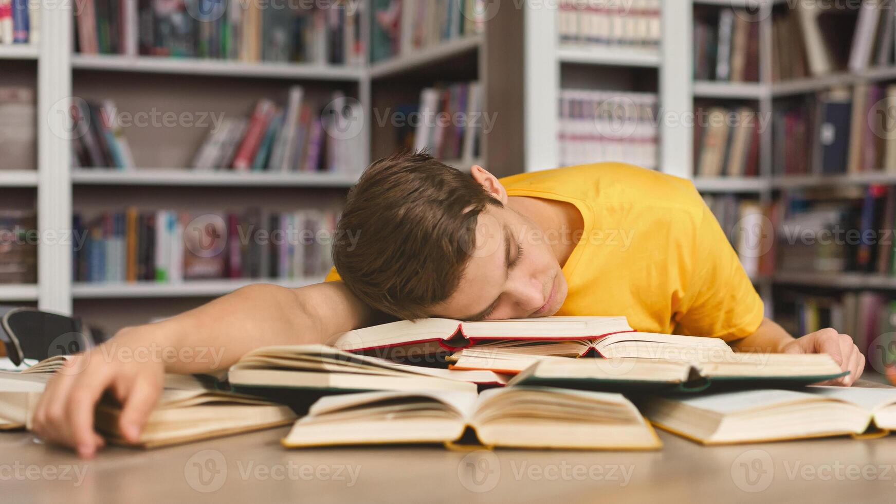 Sleeping at library. Tired caucasian guy having nap on books stack, being exhausted during preparing for exams photo