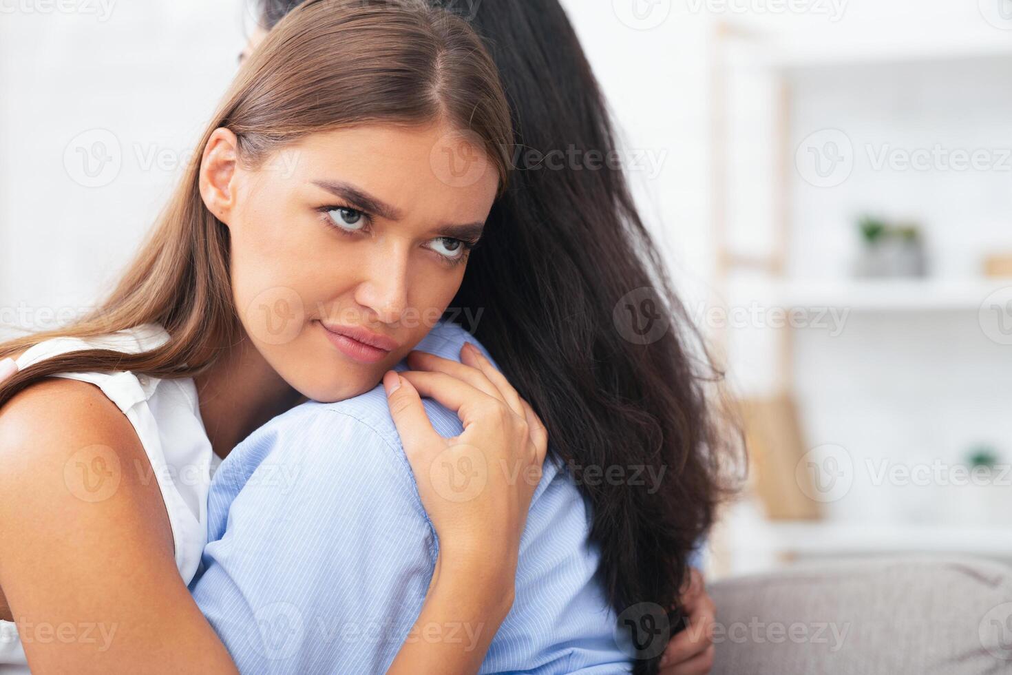 Bad Friend. Girl Rolling Eyes Embracing Crying Roommate Pretending To Be Good Sitting On Sofa At Home. Selective Focus photo