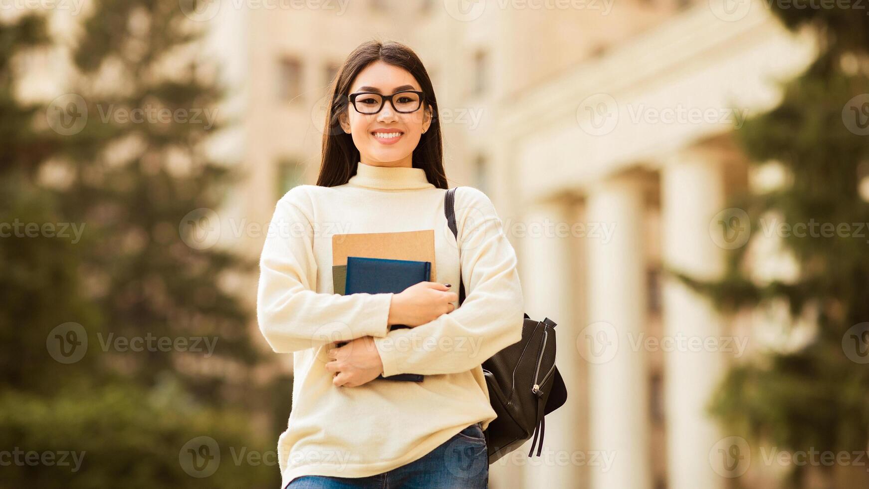 Asian woman with glasses is holding a book in her hand, looking focused and engaged in reading. She appears attentive and absorbed in the content of the book she is holding. photo