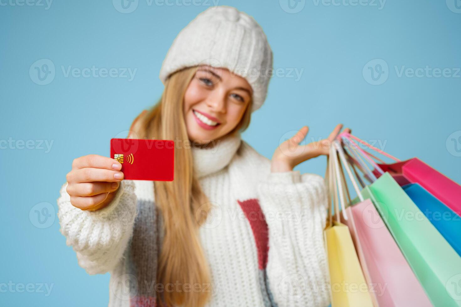 Happy young woman in white hat recommending credit card, posing with colorful shopping bags and smiling at camera, yellow background photo