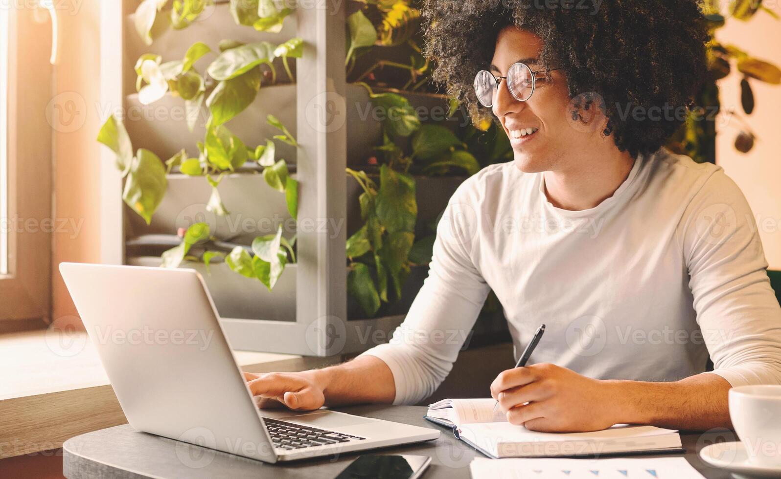 Black millennial guy working in cafe, browsing on laptop and taking notes, empty space photo