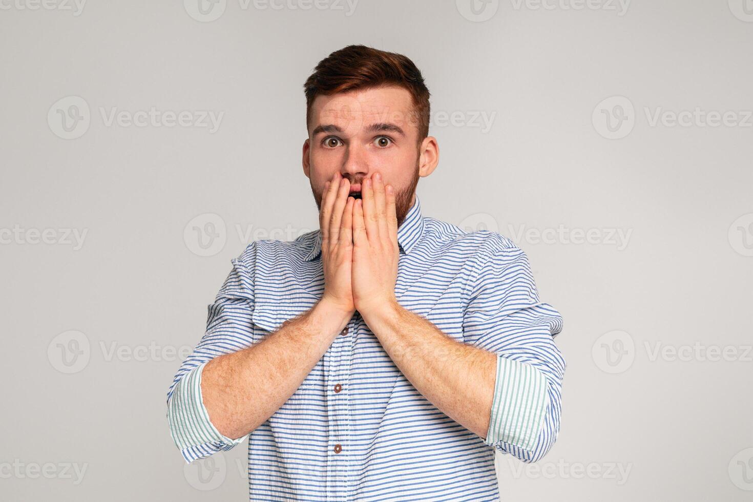 Surprised guy. Shocked man holding his hands hiding open mouth on grey studio background, copy space photo