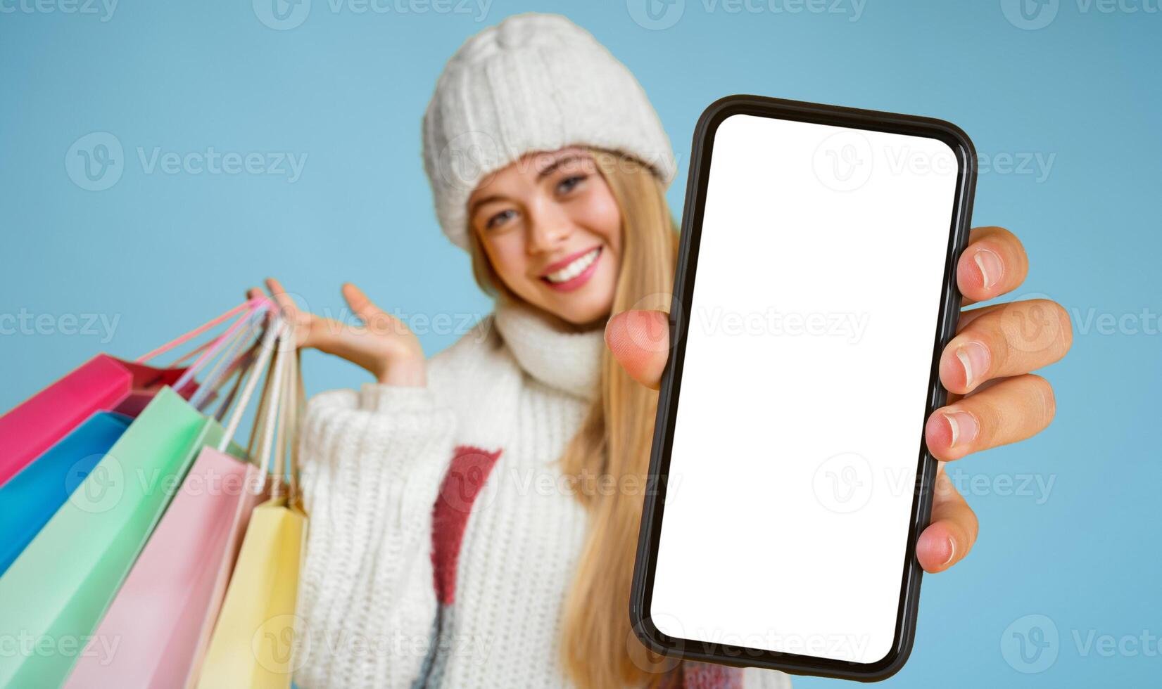 Happy young woman in white hat recommending credit card, posing with colorful shopping bags and smiling at camera, yellow background photo
