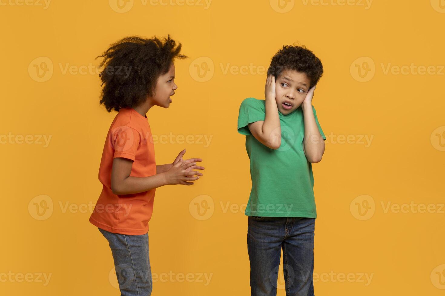 African American young girl appears to be talking animatedly to a boy, who is covering his ears with his hands, possibly indicating he is not interested in hearing what she has to say. photo