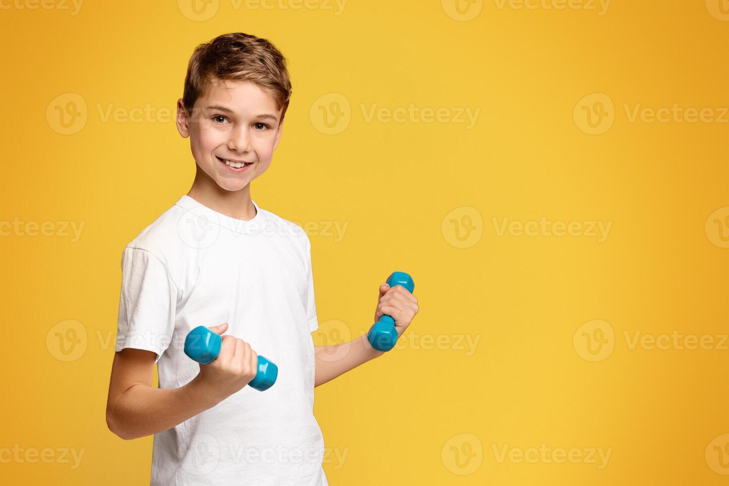 Benefits of physical training. Cheerful boy exercising with dumbbells, orange panorama background with empty space photo