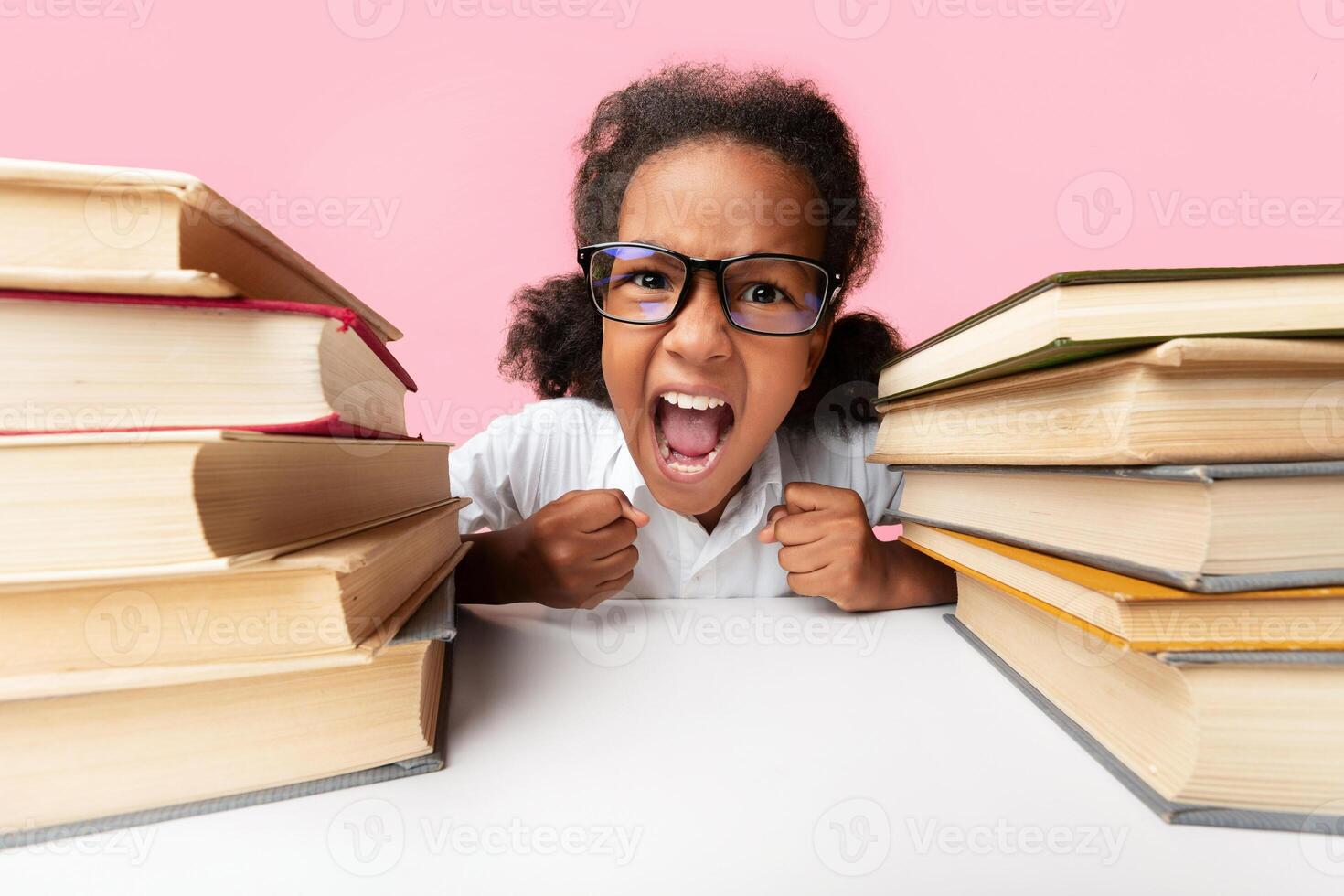 Stressed Black Elementary Student Girl Yelling Sitting Between Book Stacks In Studio Over Yellow Background. Schoolwork Overload Concept photo