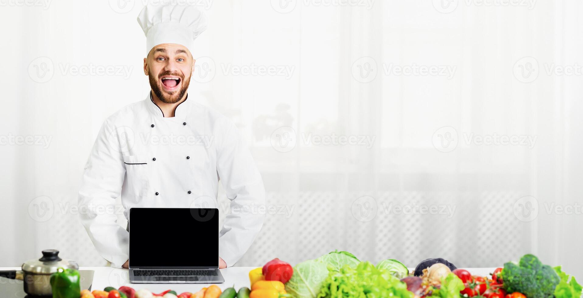Excited Male Chef Showing Laptop Computer Empty Screen Cooking Standing In Kitchen. Mockup photo