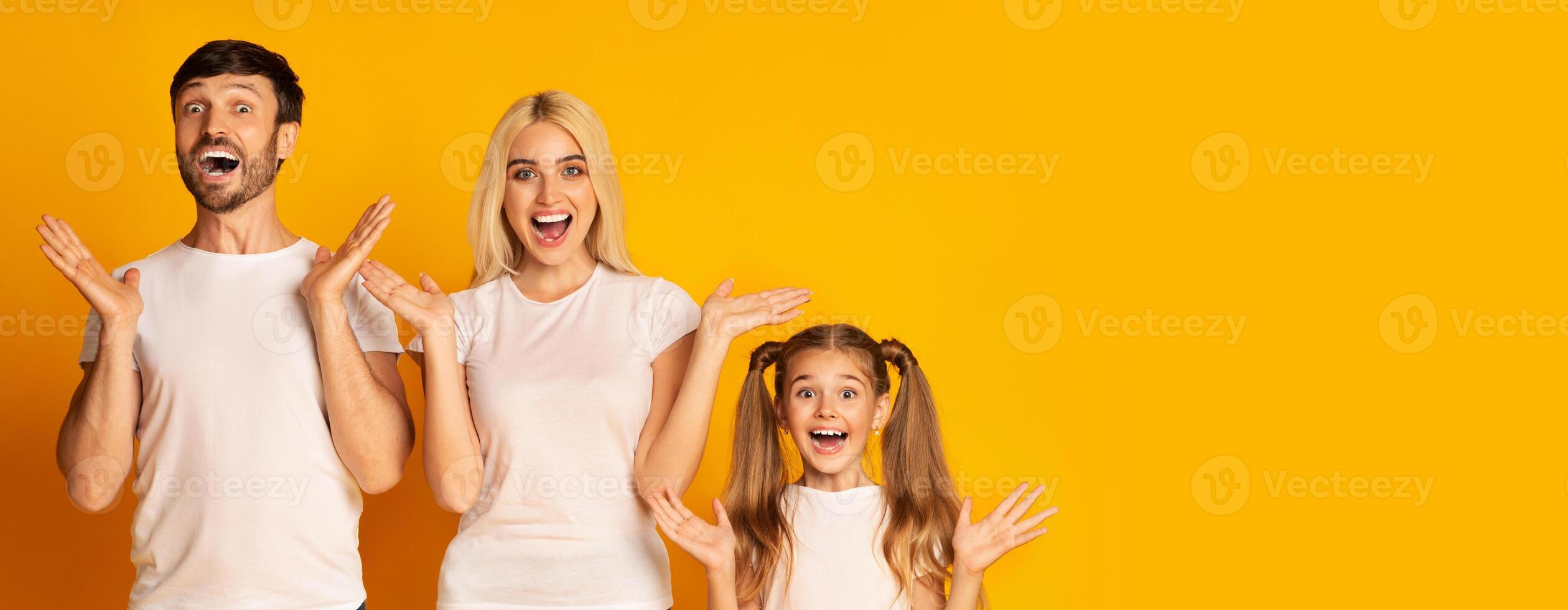 A joyful family stands in front of a vibrant yellow backdrop, with each member expressing excitement and happiness through wide smiles and raised hands, copy space photo