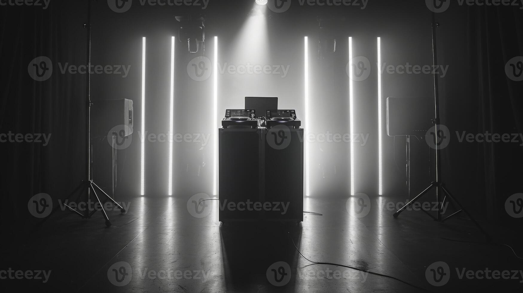 A DJ setup is illuminated with neon lights in a dark studio. The space is set with speakers on stands at either end. photo