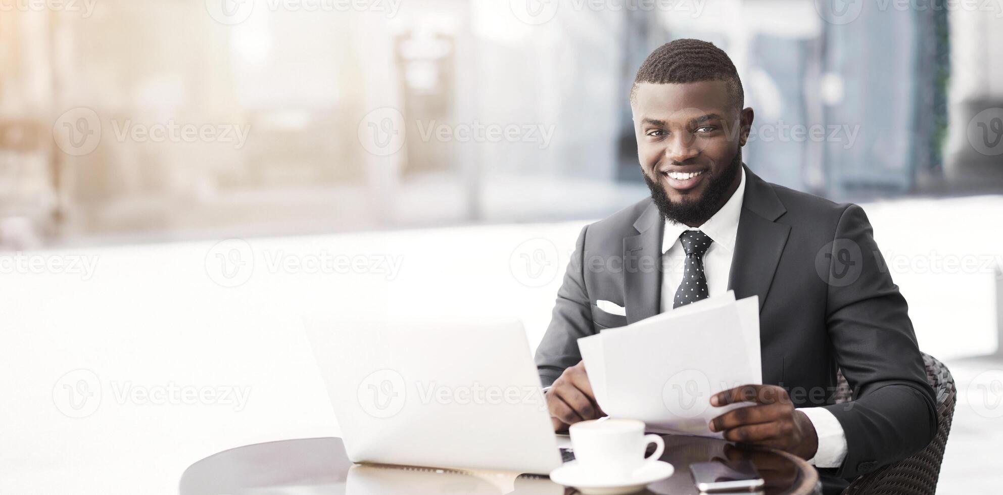Positive Afro Businessman Working With Papers And Laptop In Outdoor Cafe. Selective Focus, Free Space photo