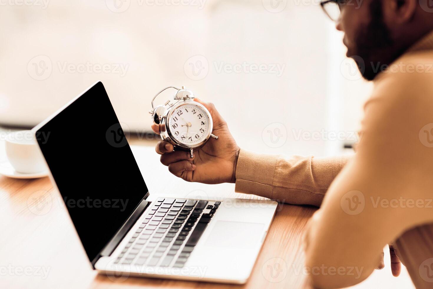Deadline Concept. Black student holding alarm clock, working on laptop. Empty space, mock up photo