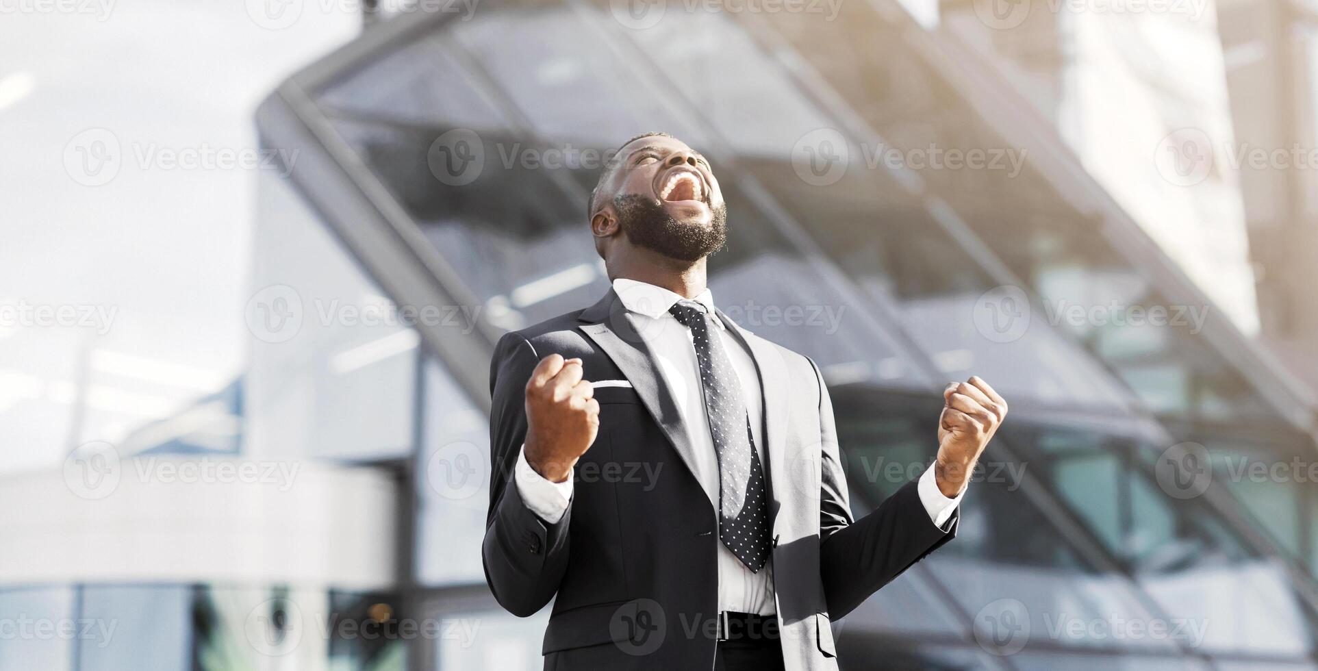 Business win. African american businessman shaking fists celebrating success at work in urban area. Copy space photo