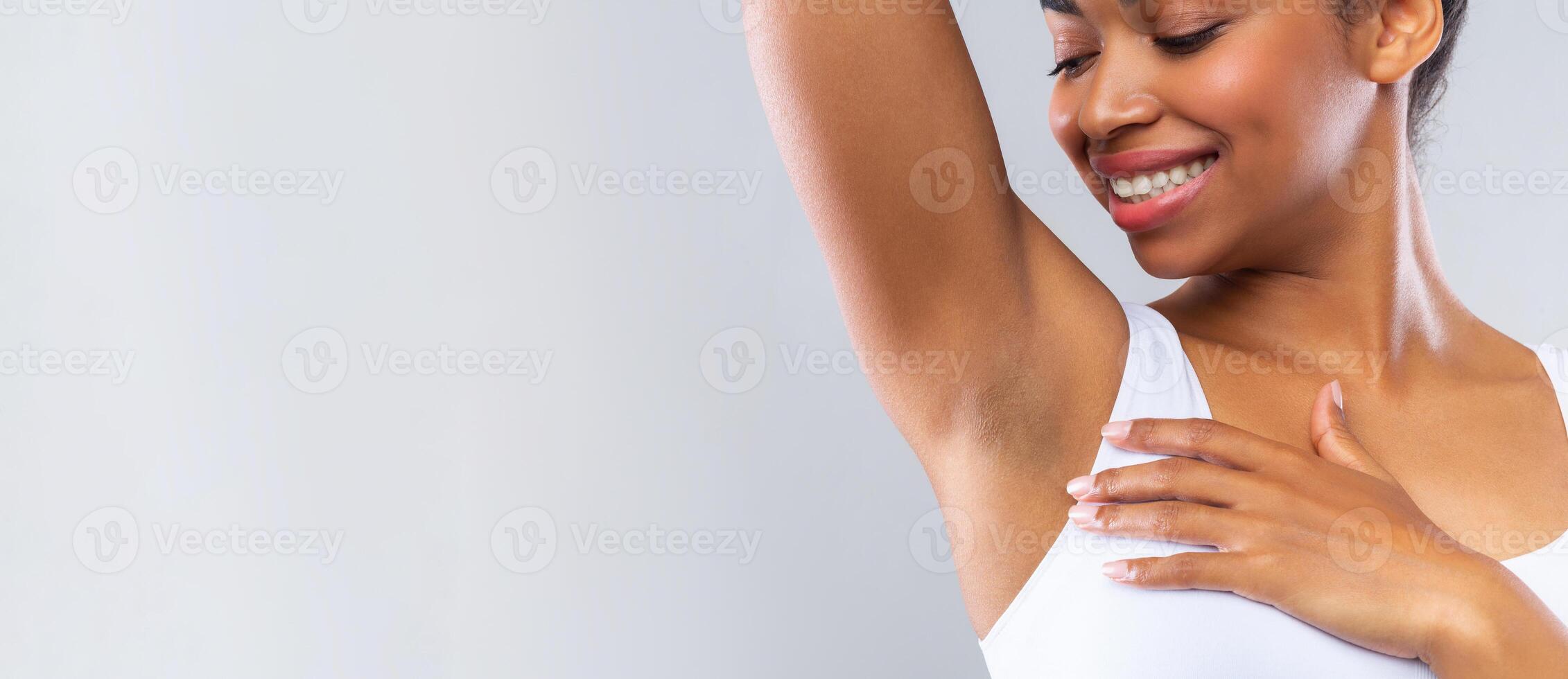 Close up of happy afro woman smelling her armpit over grey background photo