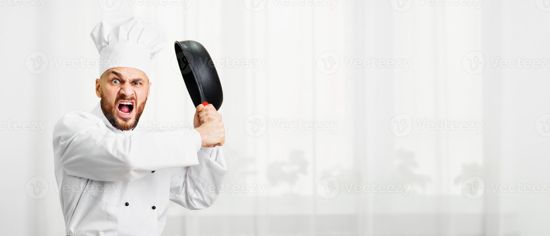 Angry Chef Man Raising Pan Threateningly Shouting Standing Next To Work Table With Vegetables In Restaurant Kitchen. Copy Space photo