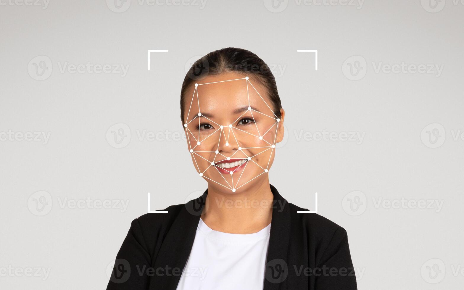A smiling Asian woman in a black blazer poses with a facial recognition graphic displayed on her face. photo