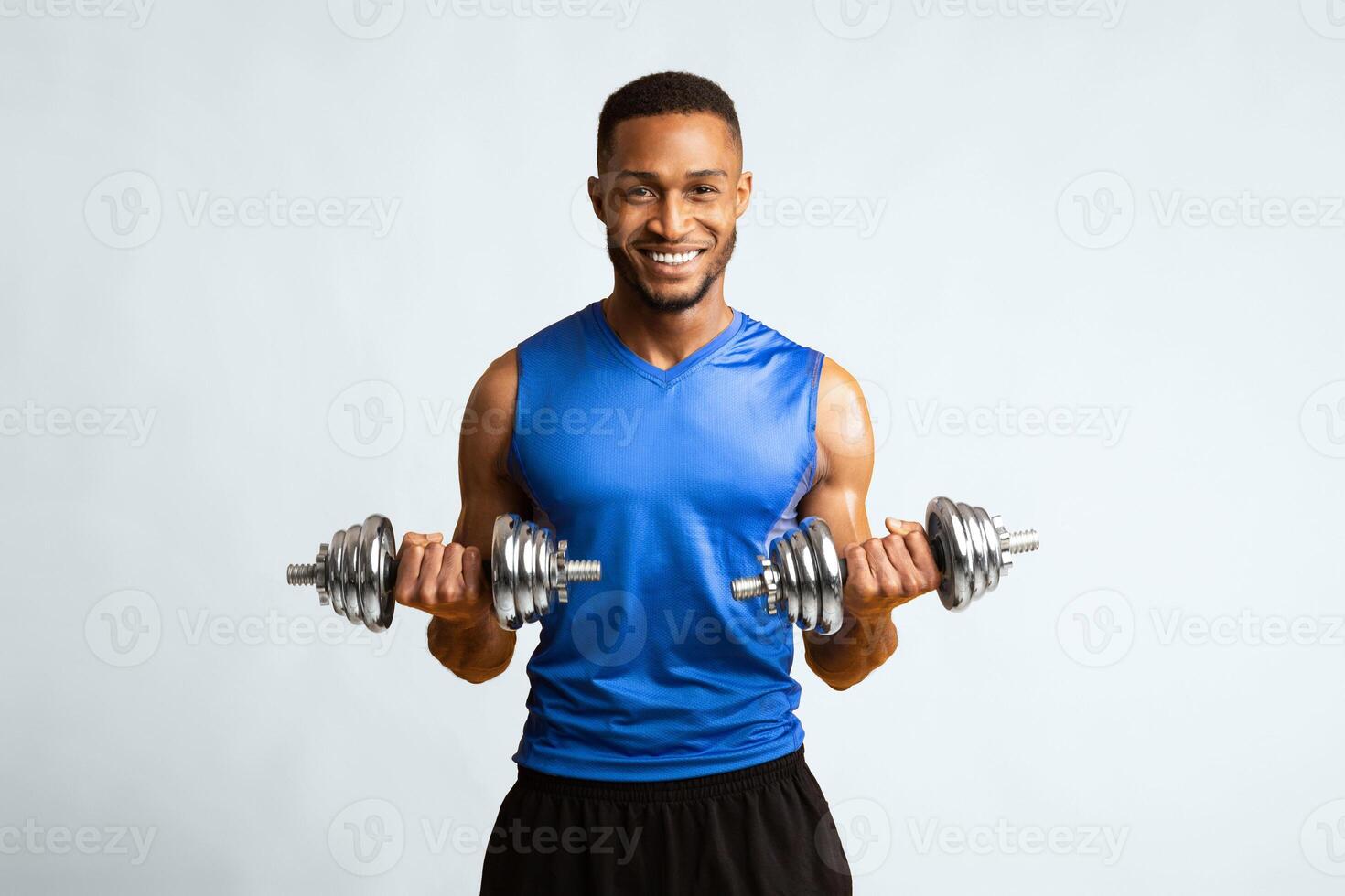 Faster And Stronger. Happy black guy doing dumbbell biceps curl isolated over orange studio wall, copyspace photo
