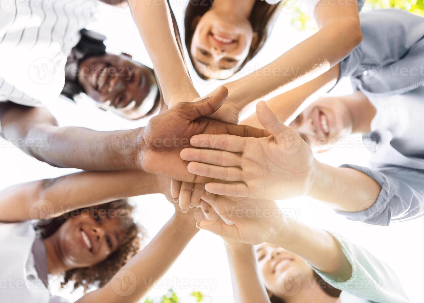 Student Friendship. Portrait of happy university friends stacking hands together, showing unity and togetherness, low angle view, selective focus photo