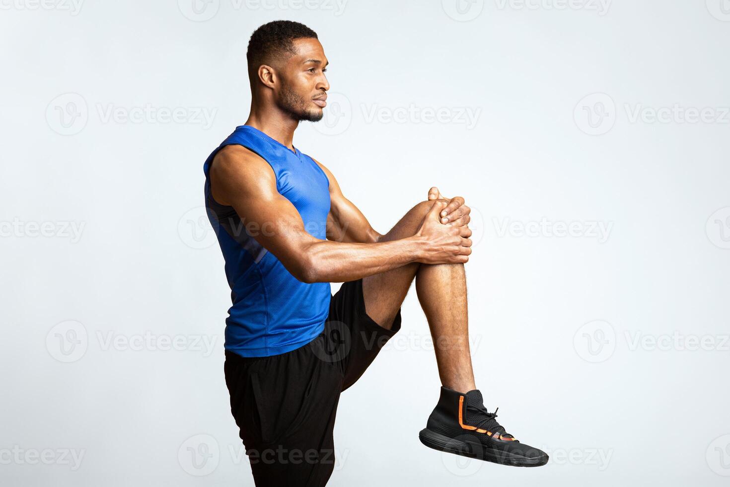 Warm Up. Side view of afro man doing high knees exercise, lifting leg over yellow background, copyspace photo