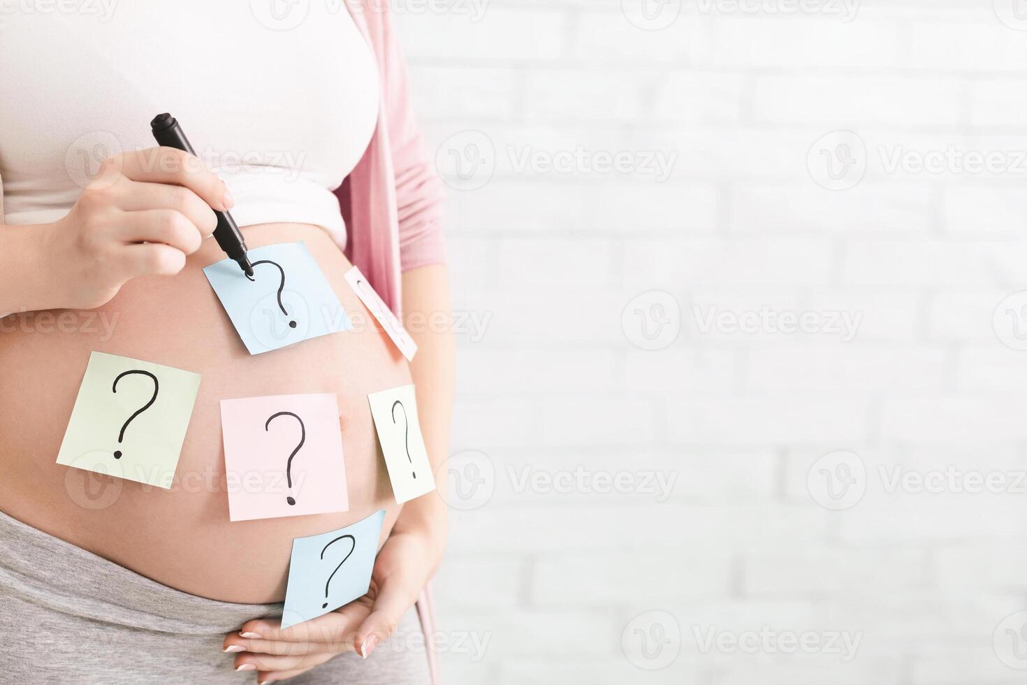 Concept of choosing baby name. Pregnant woman with question marks on paper stickers on tummy, panorama with empty space photo