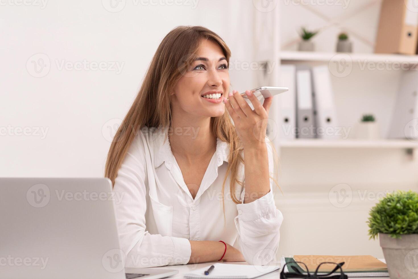 Successful Business Woman Using Smartphone Voice Assistant Sitting At Laptop In Modern Office. Entrepreneurship Concept photo