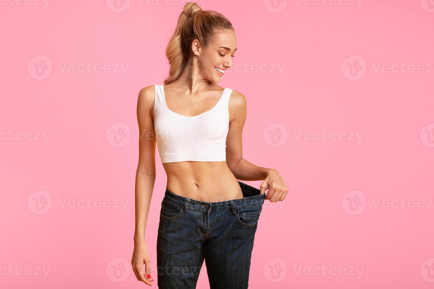 Slim Young Woman In Oversize Jeans Posing Over Yellow Background. Sport And Weight Loss. Studio Shot, Empty Space photo