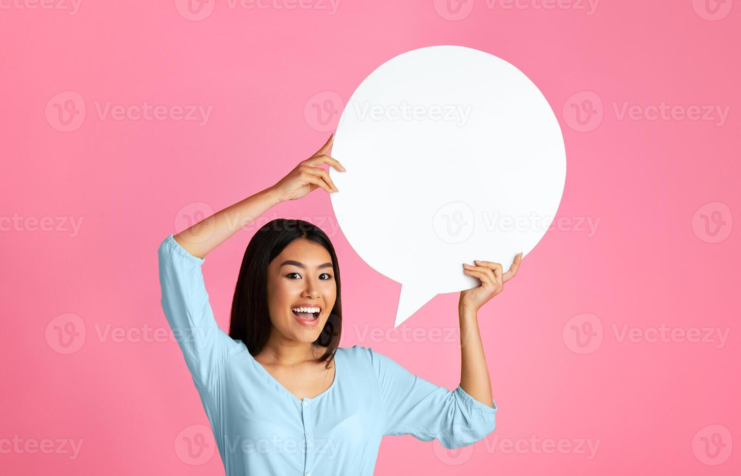 A young Asian woman with long black hair is smiling and holding a large, blank speech bubble in front of a pink background photo