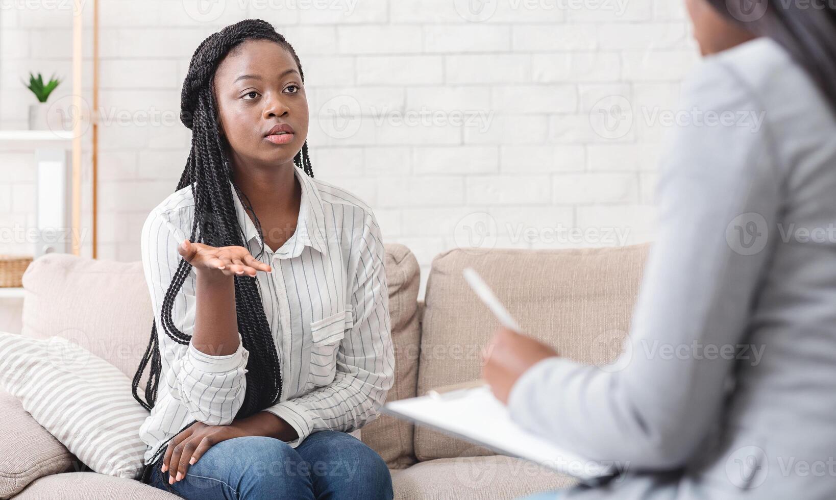 Psychotherapy concept. Sad afro lady sharing her problems at counselor's office, sitting on couch and emotionally telling something photo