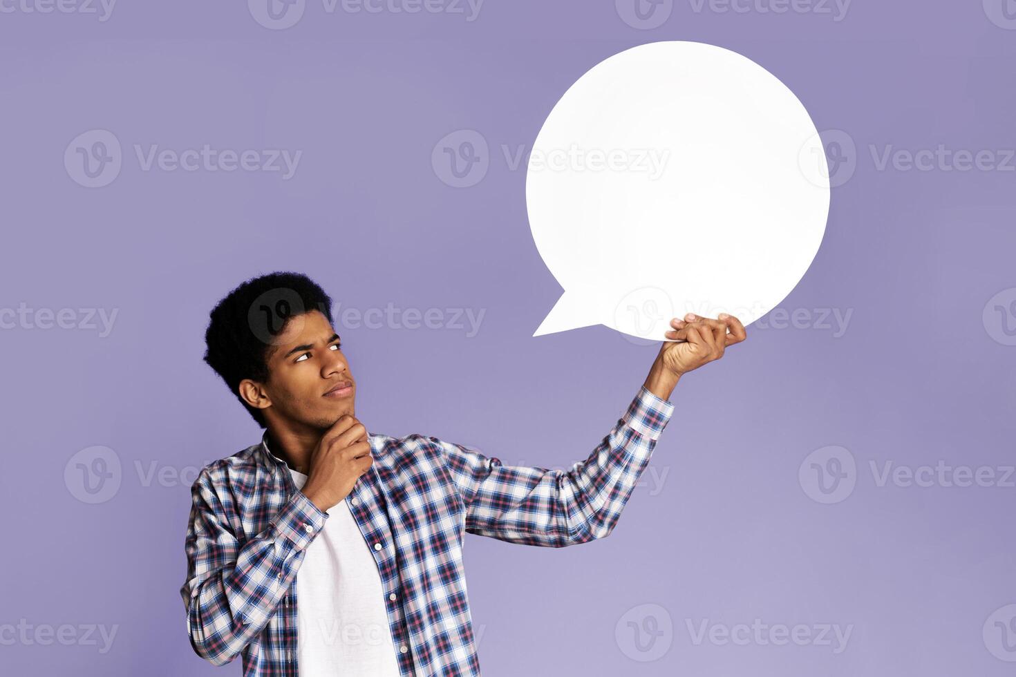 Pensive afro guy looking at blank speech bubble, touching his chin, copy space, pink background photo