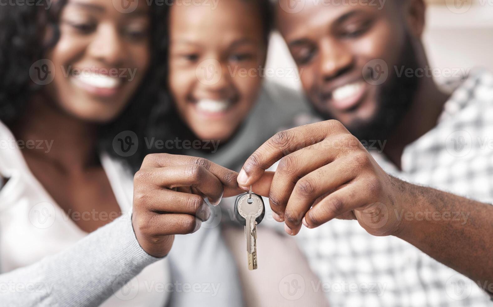 Housing concept. Happy black family with daughter holding keys from their new home, selective focus on hands, closeup. photo