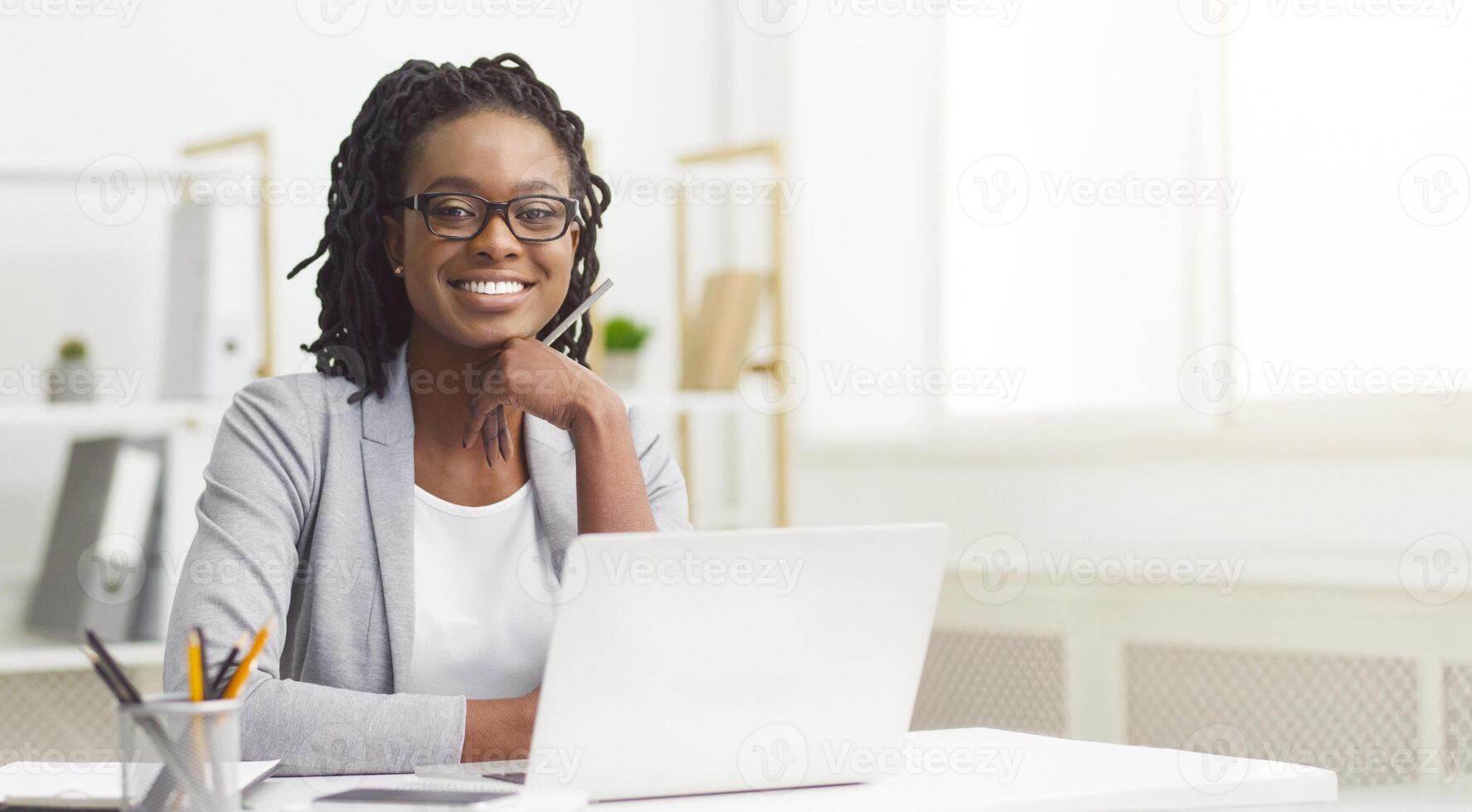 Black woman office worker is typing on her computer in a cubicle. The mood is industrious and efficient, with an organized desk and bright workspace, suggesting productivity. photo