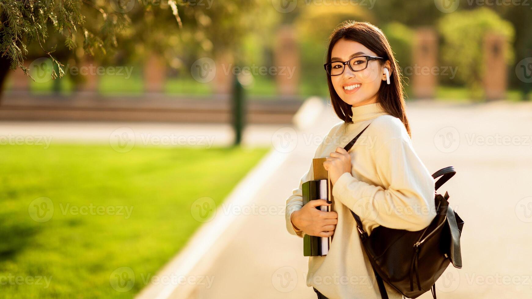 Asian woman wearing glasses and carrying a backpack is walking along a city street. She appears focused and determined as she moves forward on the sidewalk. photo
