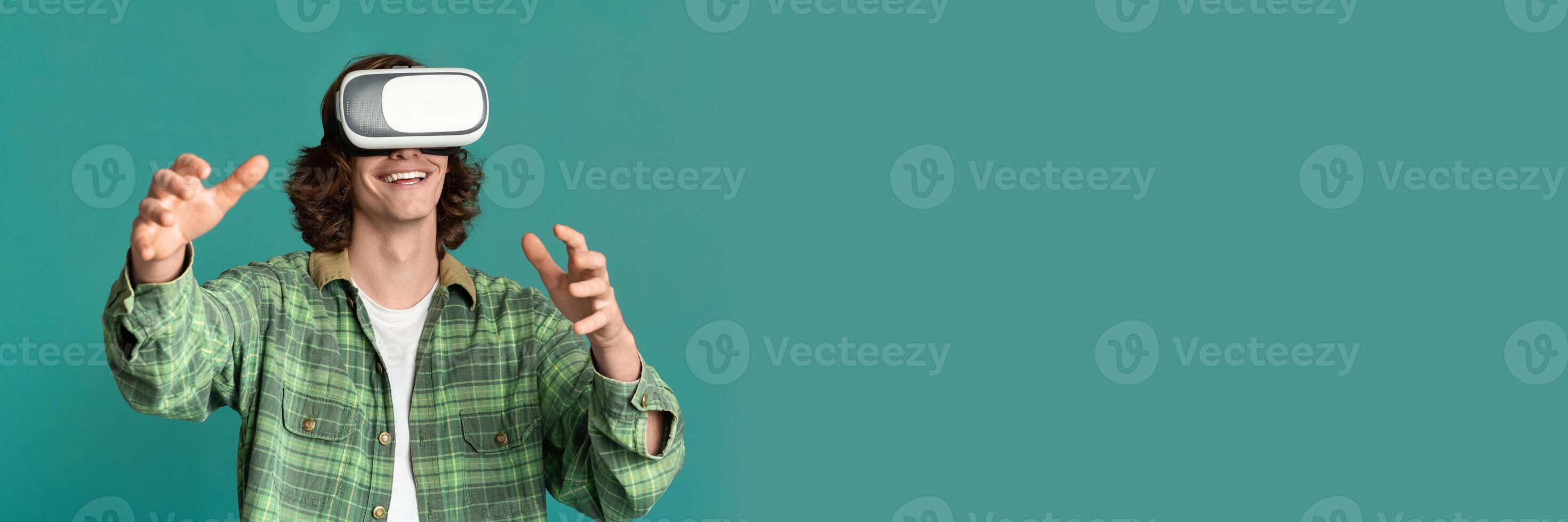 Digital world fun. Young guy in virtual reality headset playing computer games on turquoise background, copy space, web-banner photo
