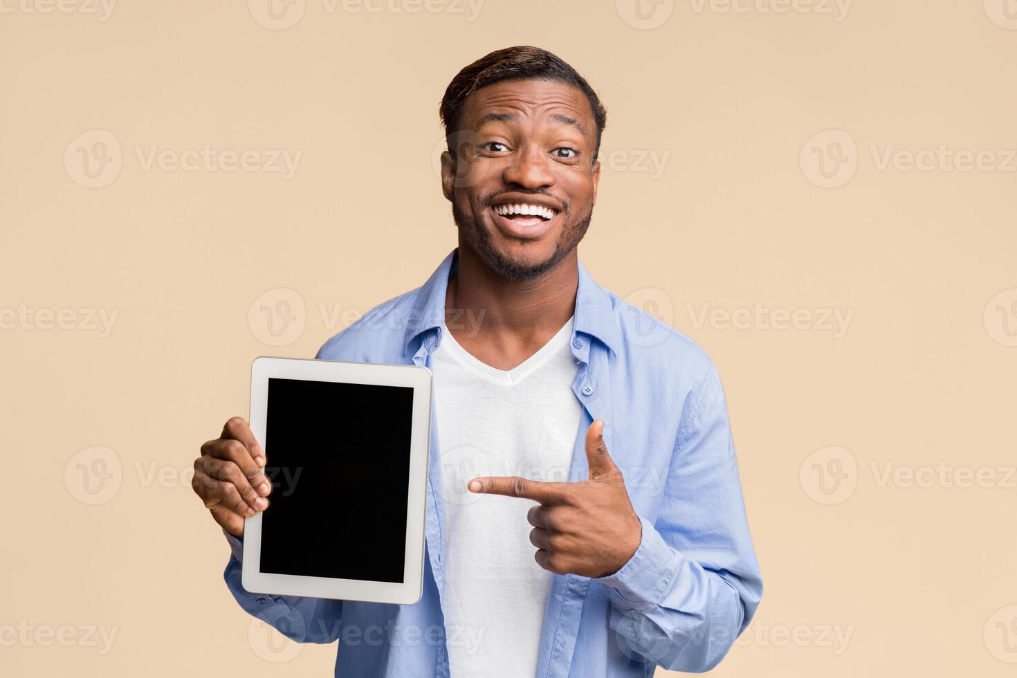 Smiling Afro Man Pointing Finger At Blank Tablet Computer Screen Standing On Yellow Background In Studio. Mockup photo
