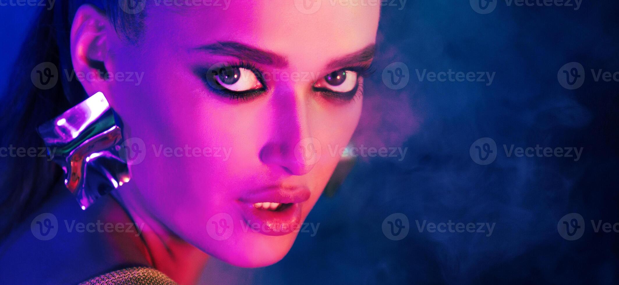A woman is depicted wearing earrings while standing in front of a solid blue background. The earrings are prominently displayed, adding a touch of elegance to the scene. photo