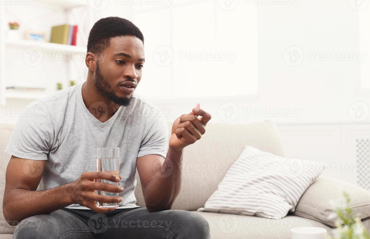 Serious african-american man ready to take a pill while sitting on a couch at home, copy space photo