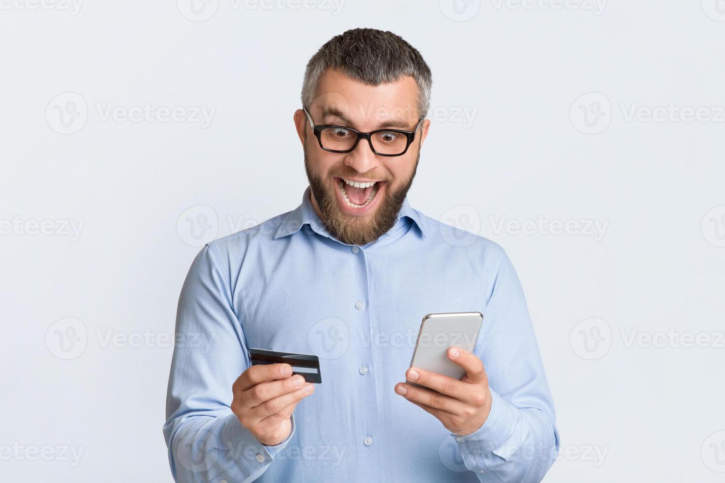 A man is seen holding a smart phone in one hand and a credit card in the other. He appears to be engaged in making a transaction or online purchase using the phone and card. photo