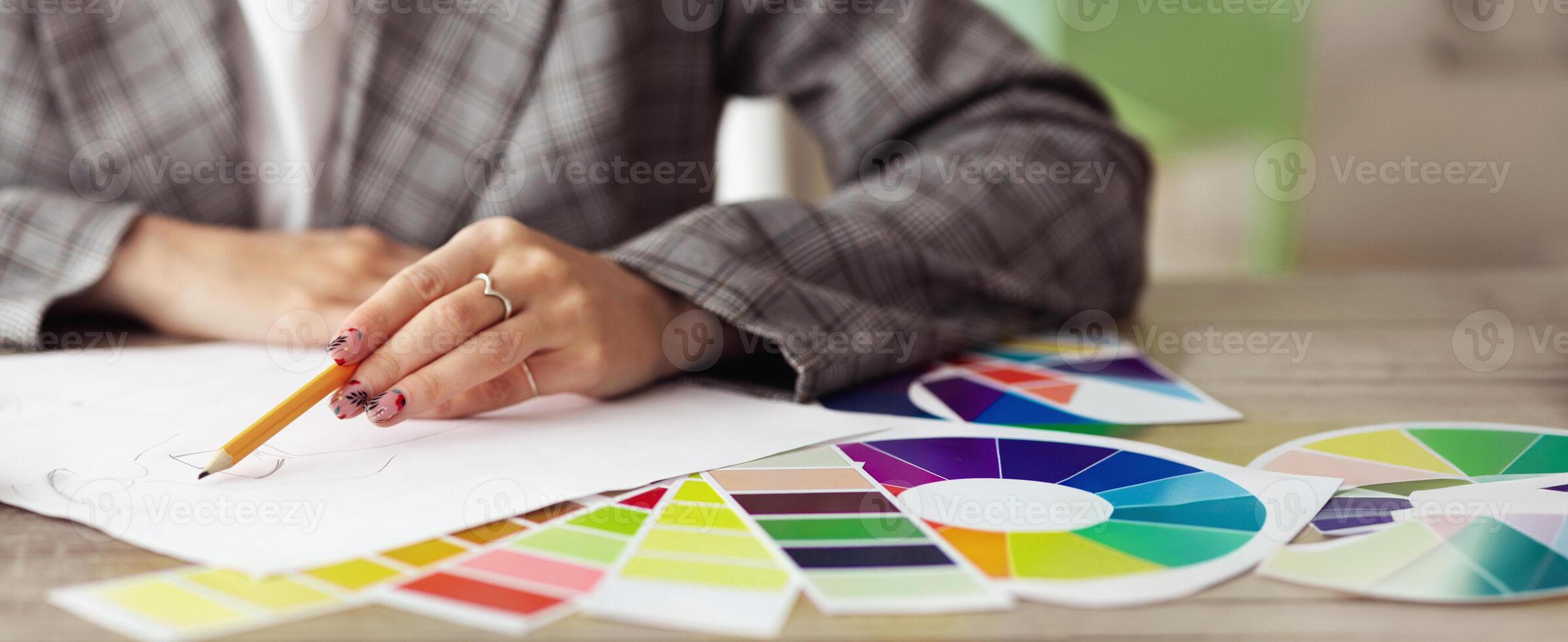 A womans hand draws on a piece of paper with a pencil, surrounded by color swatches. photo