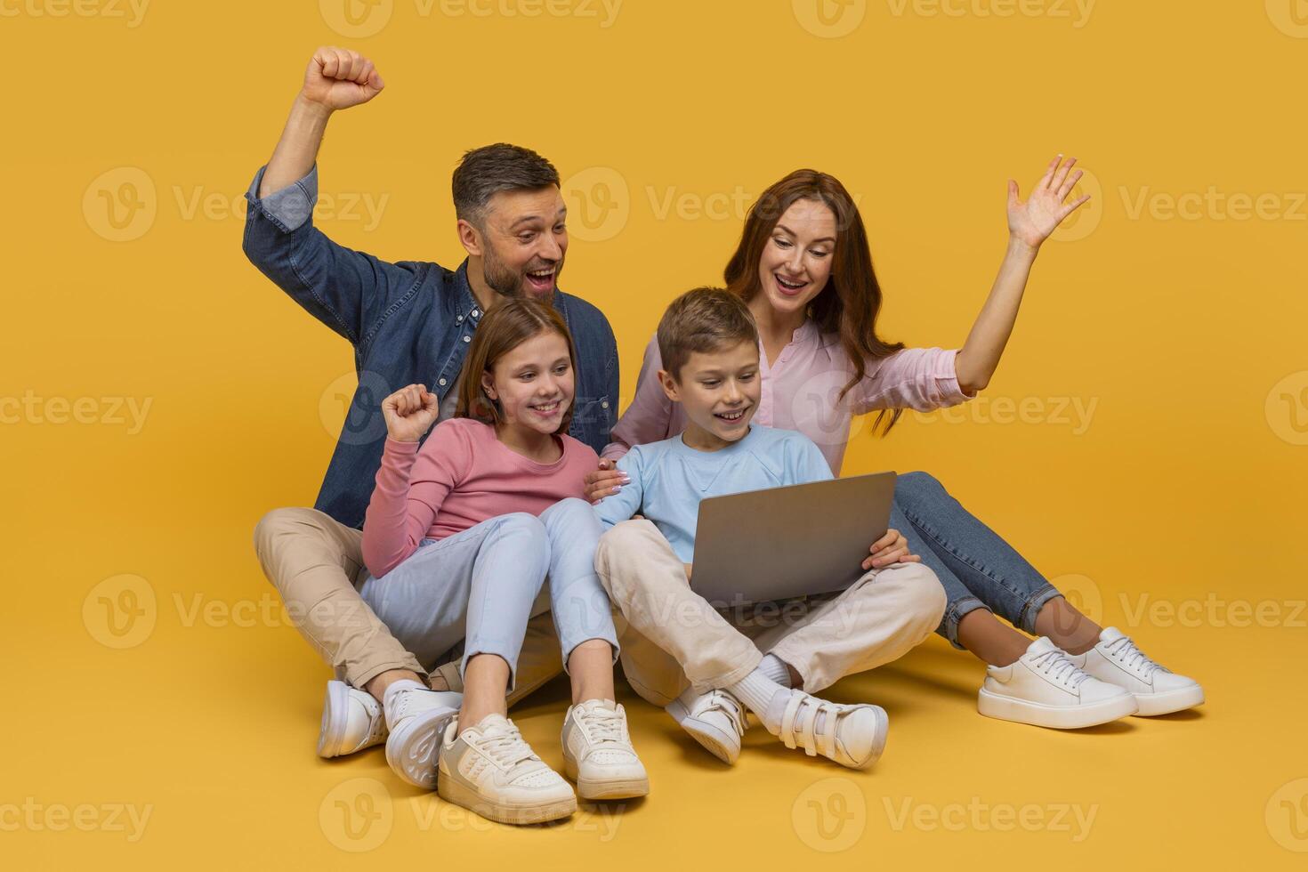 A joyous family consisting of a father, a mother, and two children are sitting together with a laptop, expressing excitement and happiness with raised fists and wide smiles photo