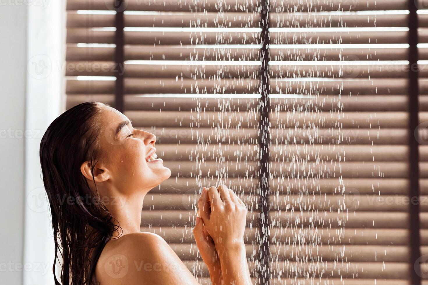 Young woman taking refreshing shower, standing under water drops, side view photo