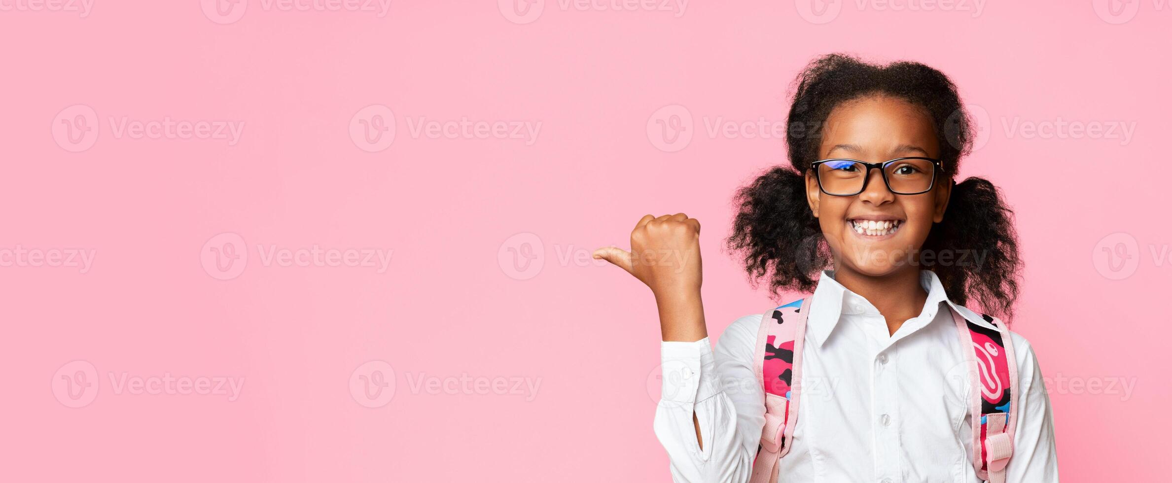 Happy Elementary Student Girl Pointing Thumb At Copy Space Recommending Educational Online Classes Standing Over Yellow Background. Panorama photo