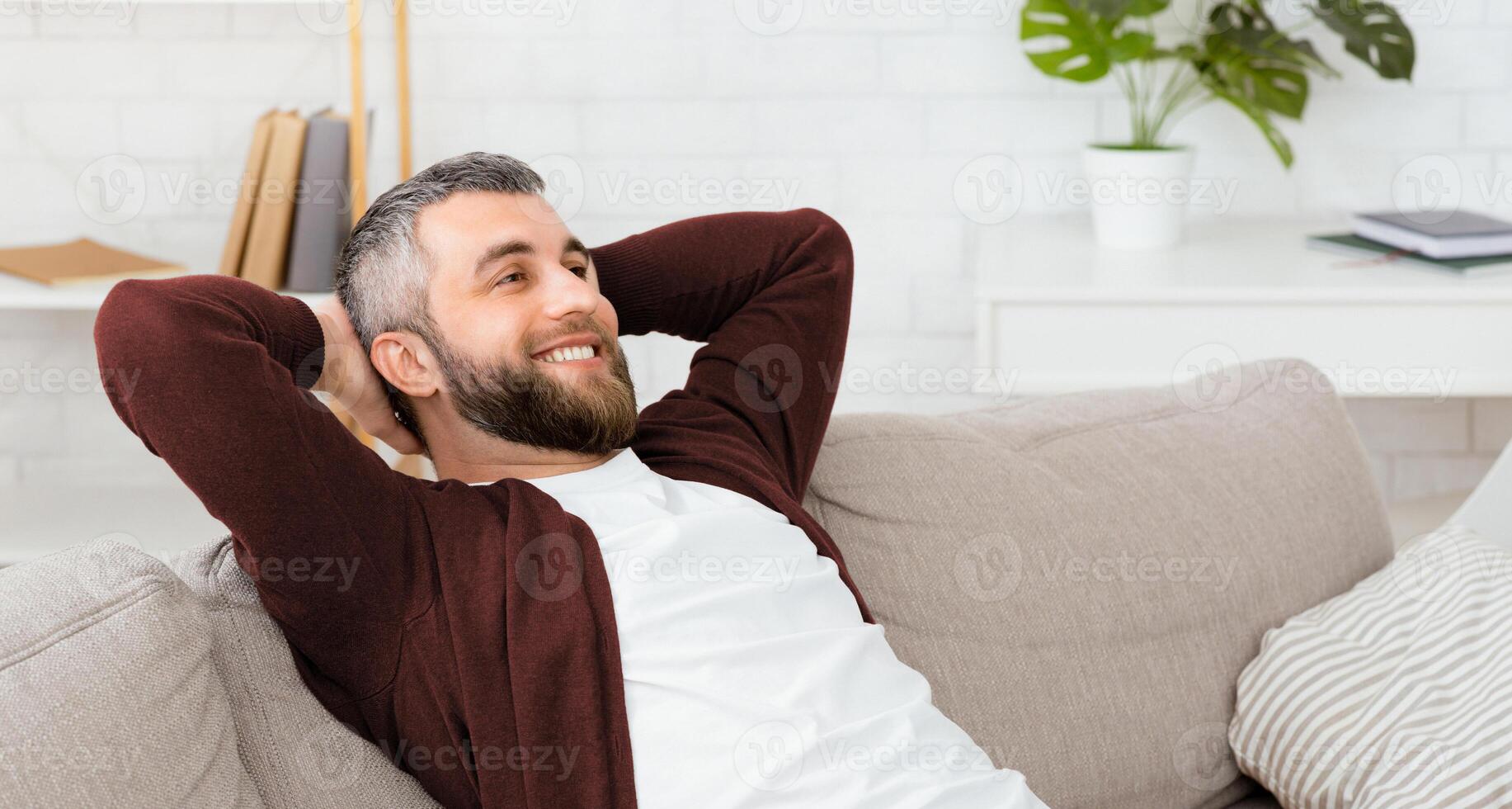 A man is sitting comfortably on a couch with his hands placed behind his head. He appears relaxed and at ease, possibly taking a moment to unwind. photo