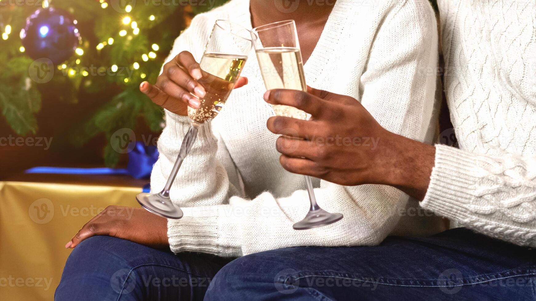 Smiling black couple holding and clinking champagne glasses, celebrating Christmas or New Year together at home near Xmas tree photo