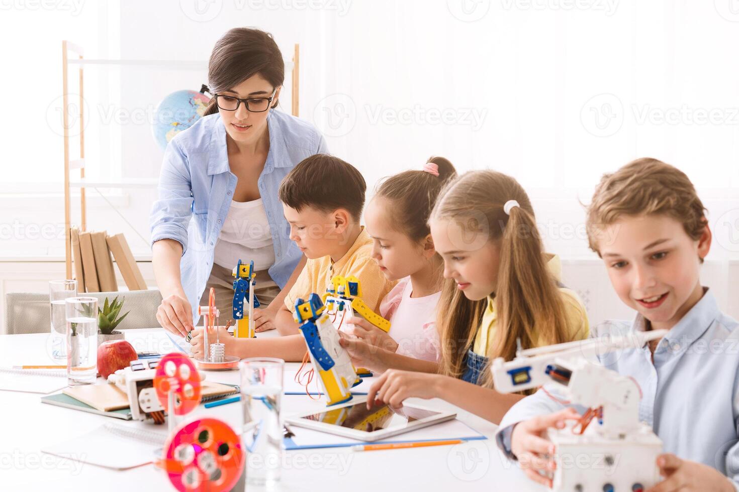 Group of young students in a classroom setting. They are learning about robotics and building their own robots. A teacher is assisting the students, who are all engaged in the activity. photo