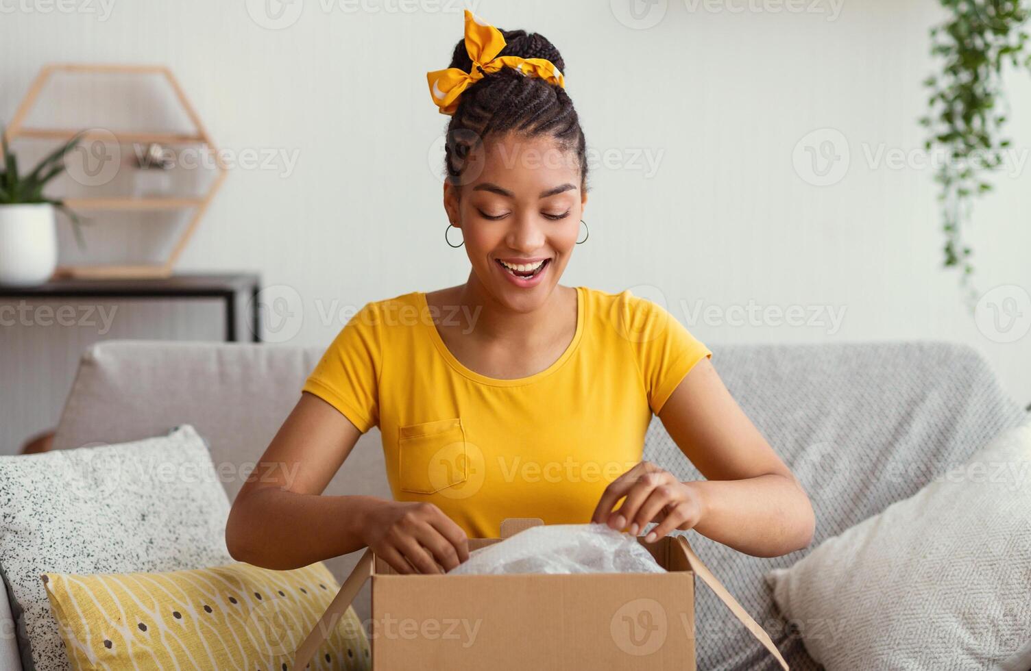 Quick Delivery Service Concept. Happy black lady received package, unpacking cardboard box, sitting on the sofa in living room at home, copy space. Female buyer satisfied with online shopping purchase photo