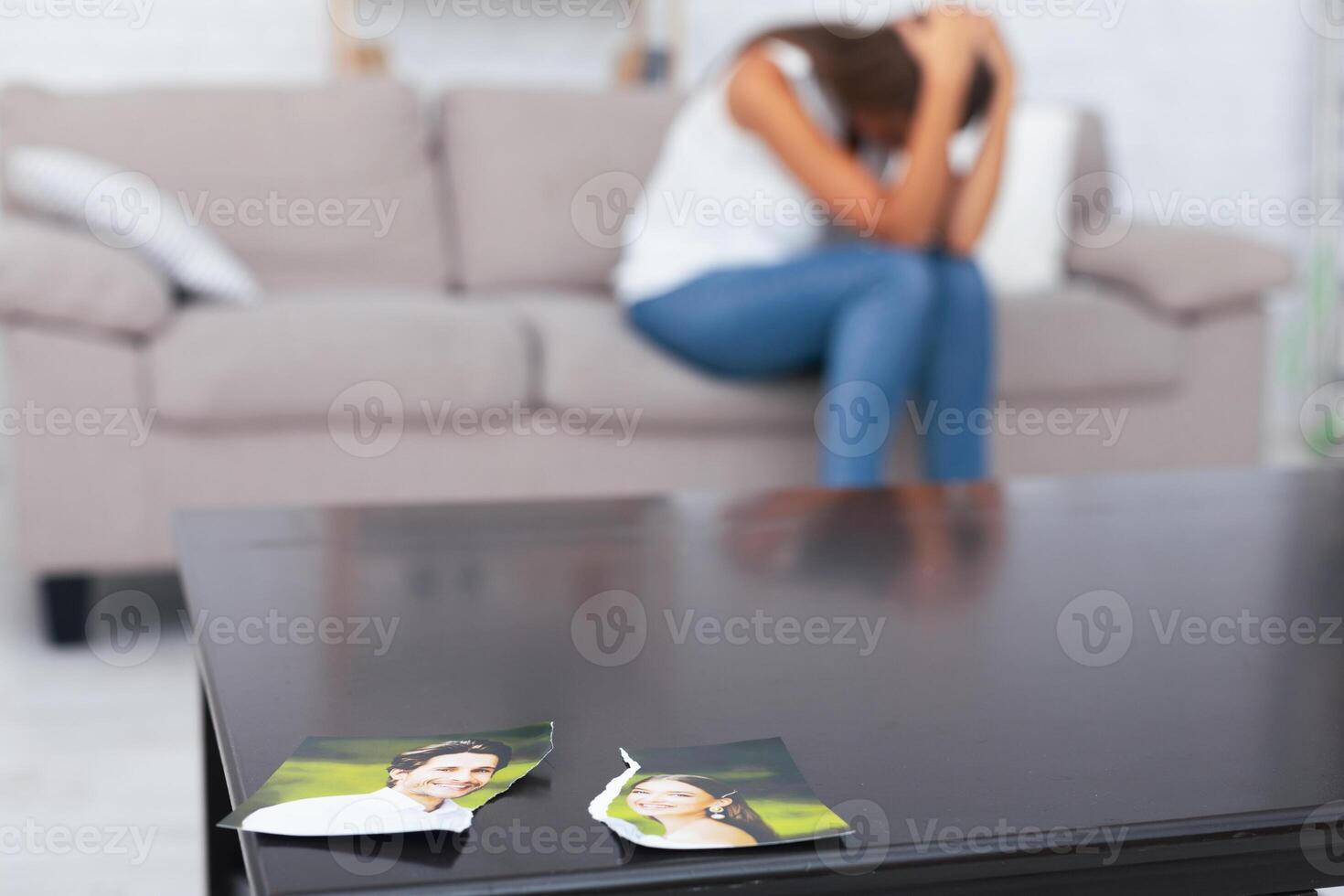 Breakup. Torn Photo Of Happy Couple Lying On Table While Unrecognizable Depressed Girl Crying Sitting On Couch Indoor.