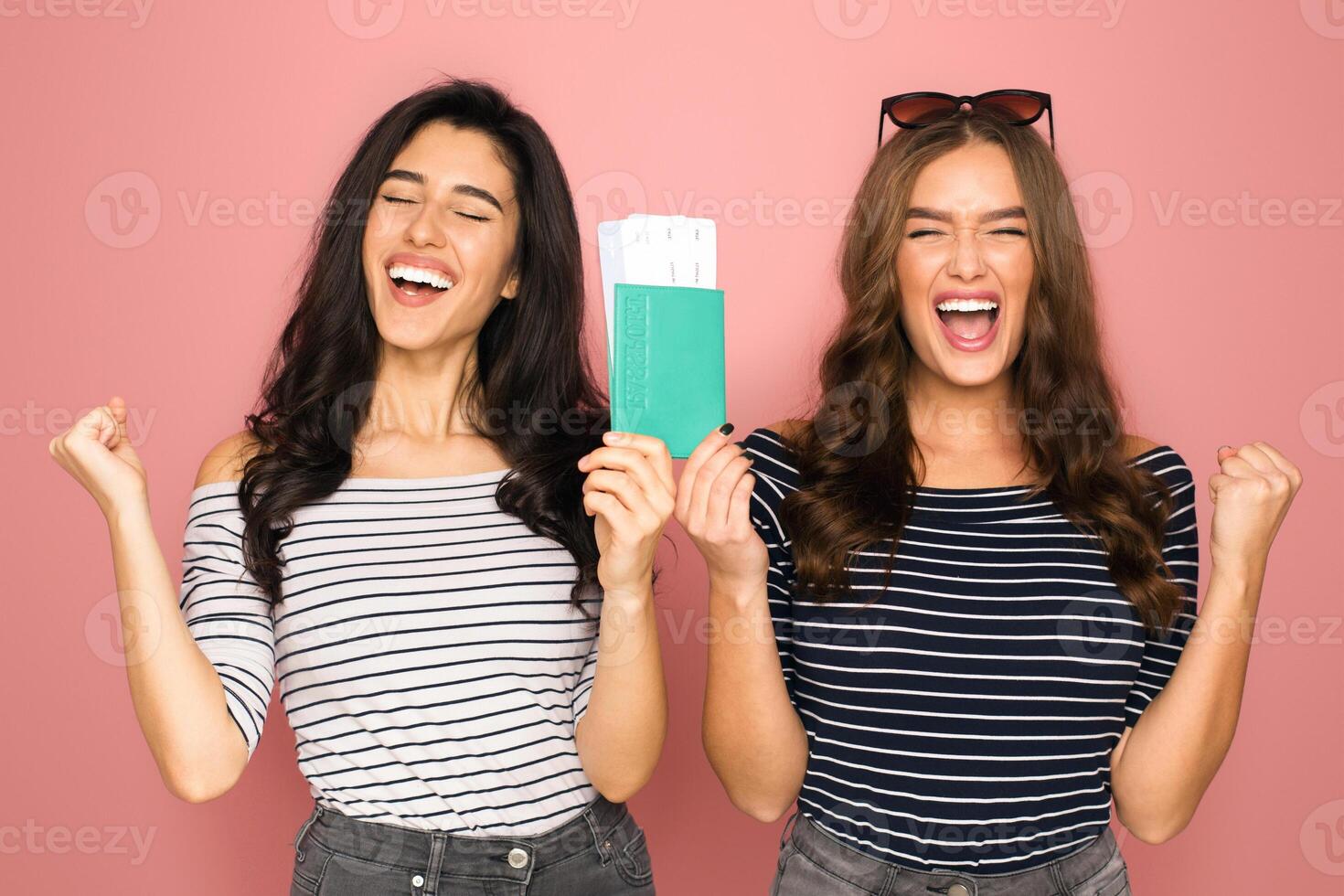 Two young women are standing shoulder to shoulder, each raising one clenched fist in a sign of excitement, holding passports and boarding passes photo