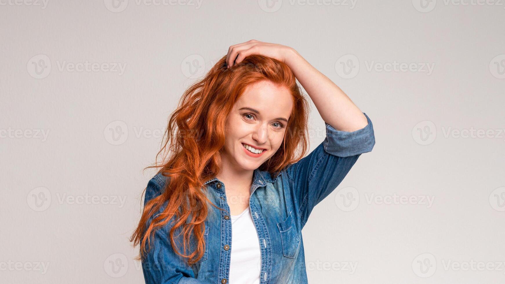 A woman with vibrant red hair is striking a pose for a picture. She is confidently displaying her unique features and style to the camera, touching head photo